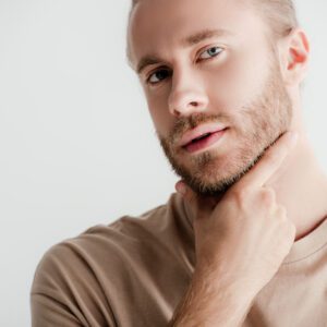 young handsome man in beige outfit touching face isolated on white