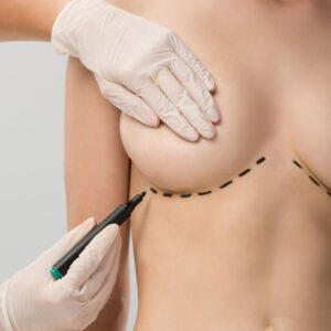 cropped view of plastic surgeon in latex gloves making marks on breast isolated on grey
