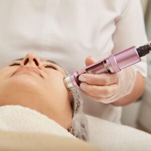 Close up of female cosmetologist hand using professional cosmetic device while performing face rejuvenation procedure