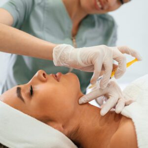 Yellow colored syringe, making injection. Woman face getting facial care by beautician hands at spa salon.